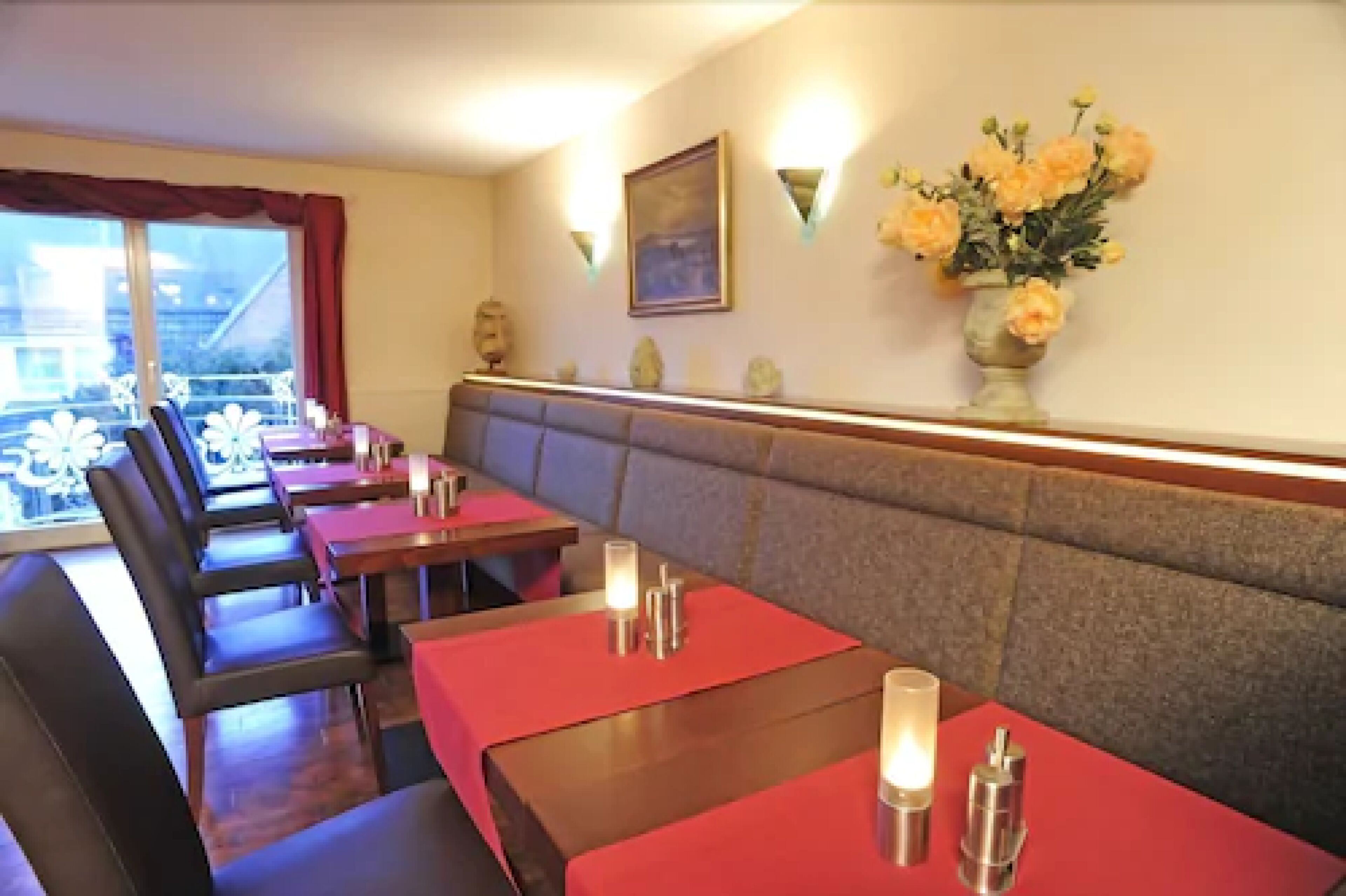 A restaurant with booths and tables, a vase of flowers on the wall, and a painting above the counter.
