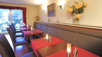 A restaurant with booths and tables, a vase of flowers on the wall, and a painting above the counter.