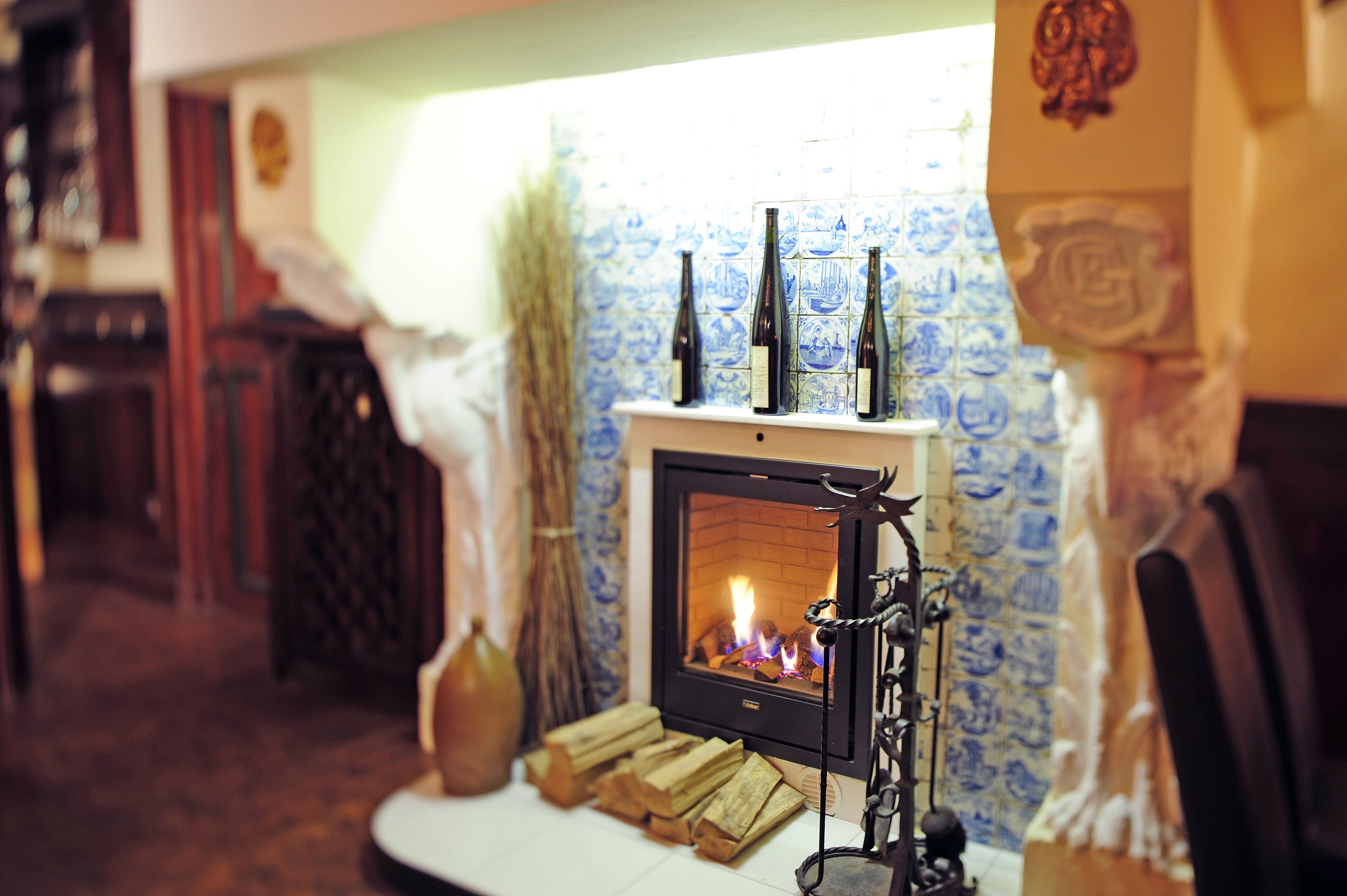 A cozy room with a fireplace, a tiled wall, and a wooden table with bottles and logs.