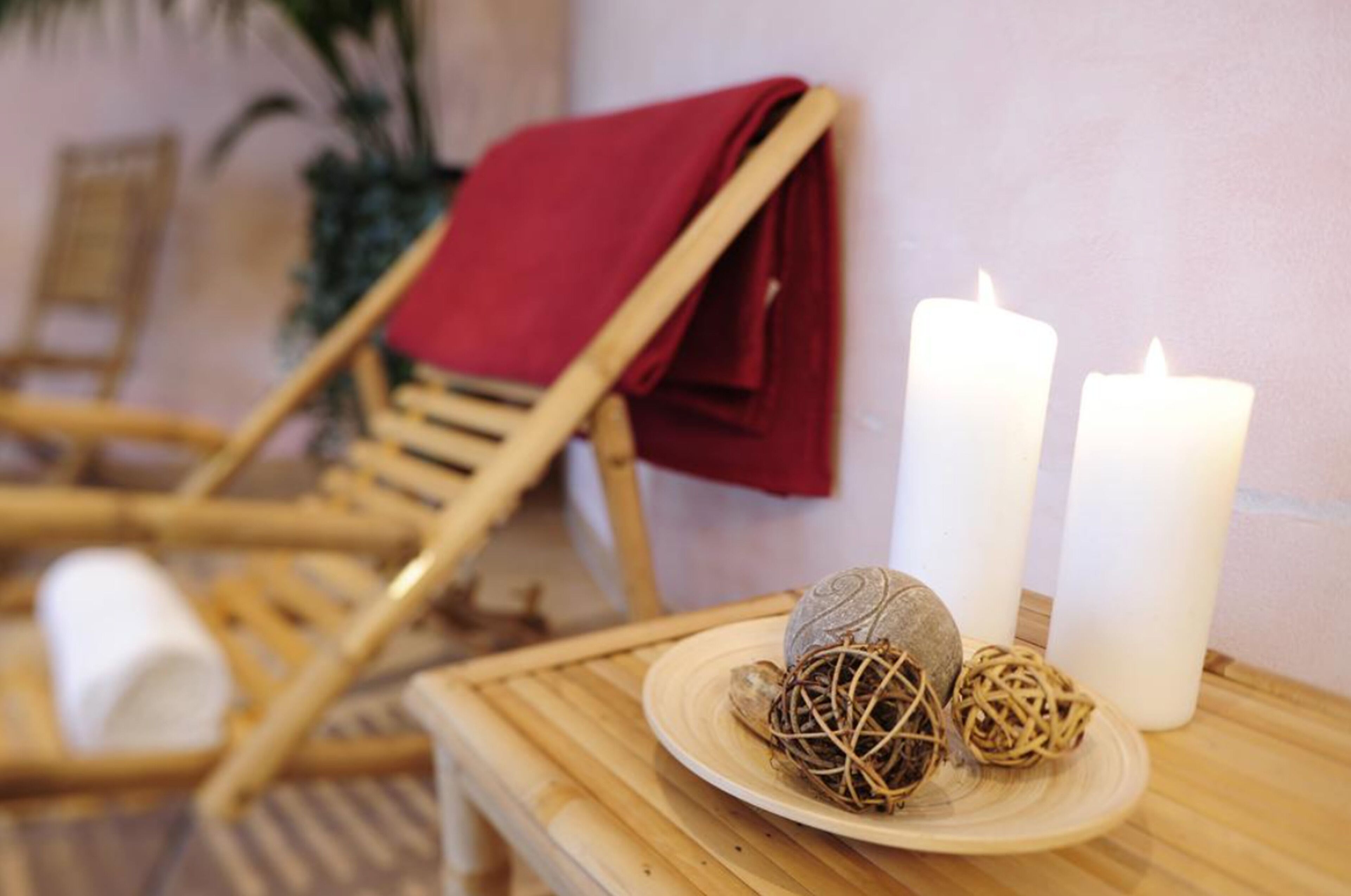 Une chaise en bois, une serviette rouge, deux bougies blanches et des boules décoratives sont posés sur une table.