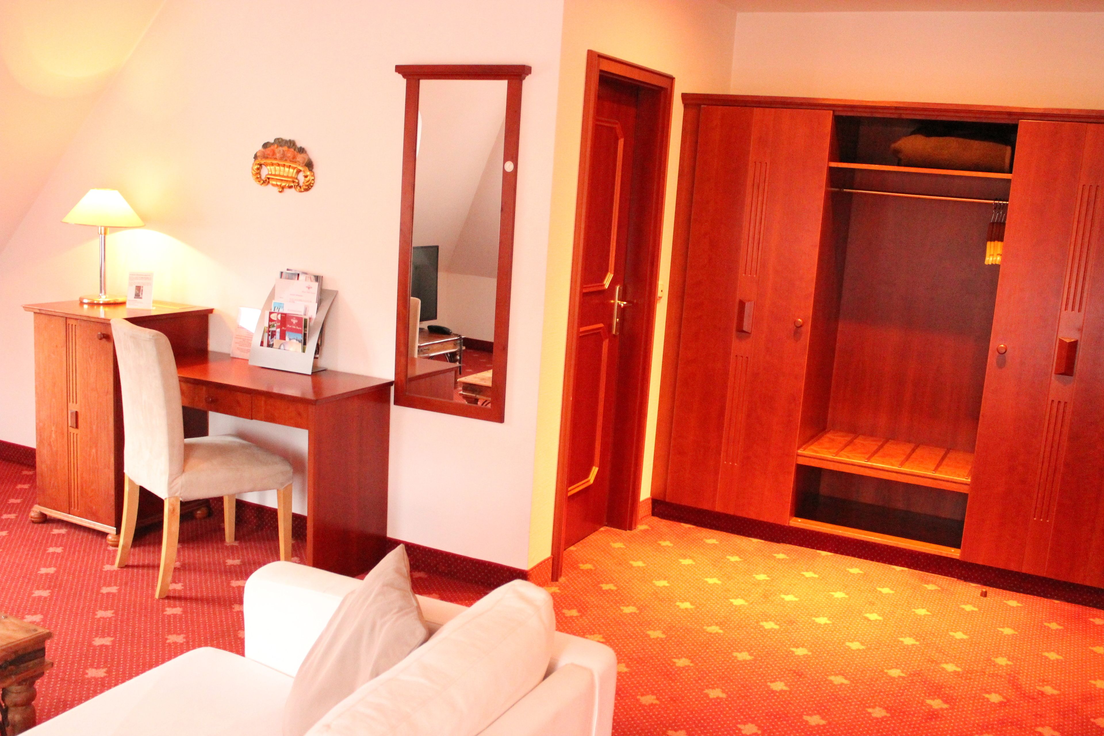 A hotel room with a desk, chair, wardrobe, and a sofa.