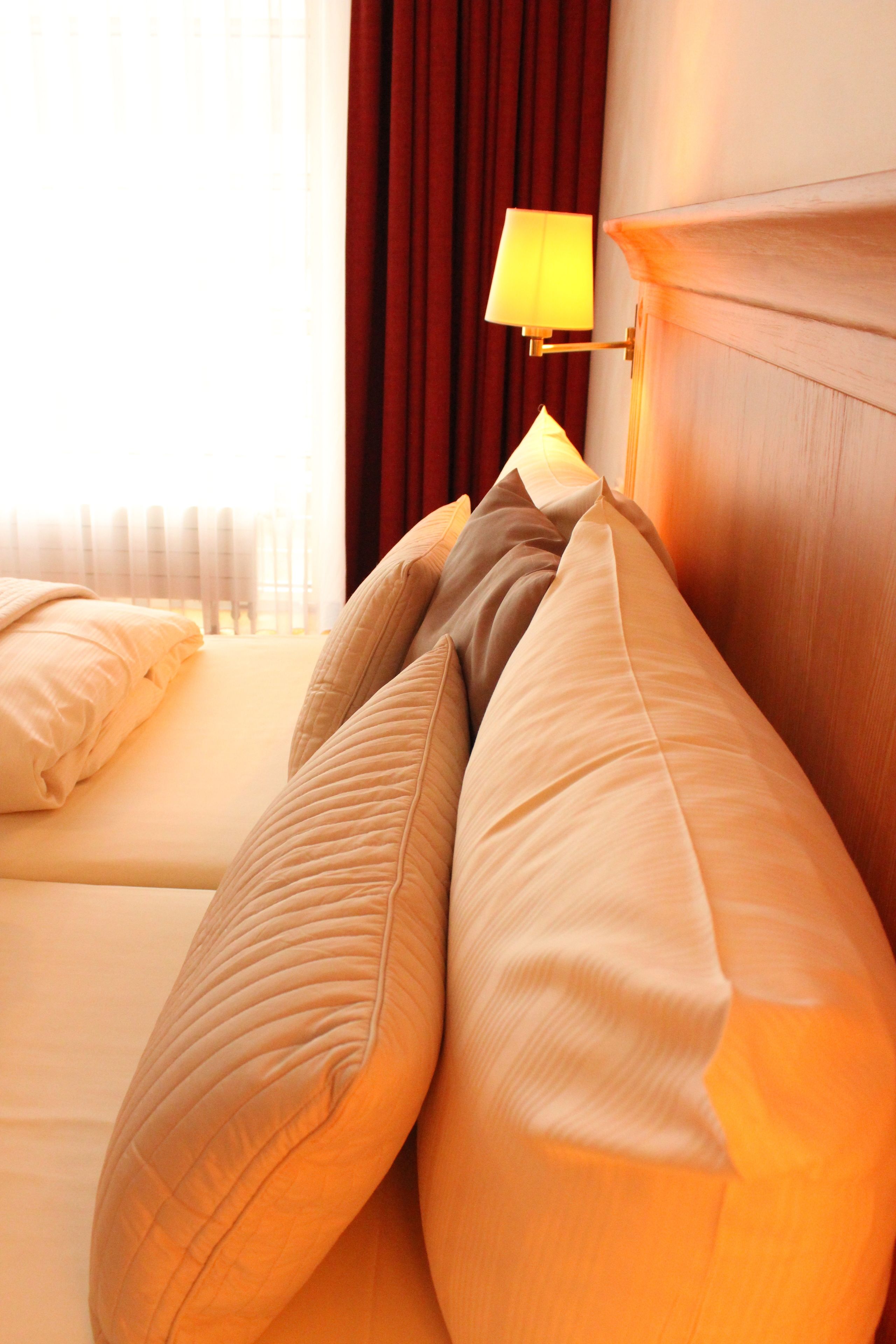 A hotel room with a bed, pillows, a lamp, and a window with curtains.
