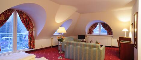 A hotel room with a bed, a sofa, a desk, and two windows with curtains.