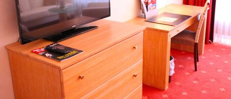 A television on a wooden dresser, a magazine on the dresser, a wooden desk, and a chair.