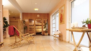 Een kamer met een houten vloer, een sauna, een houten stoel, een klein tafeltje met kaarsen en een kamerplant.