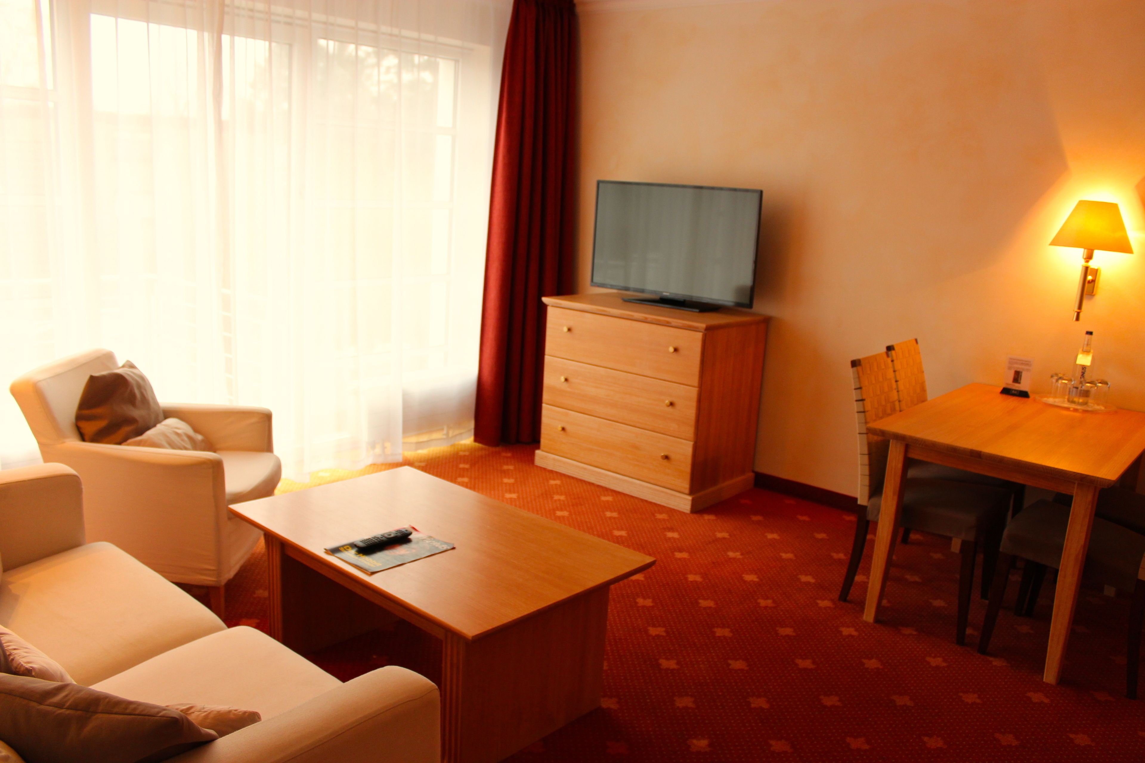 Ein Hotelzimmer mit einem Holztisch, einem Fernseher auf einer Kommode, einem Sessel, einem Tisch und einer Lampe.