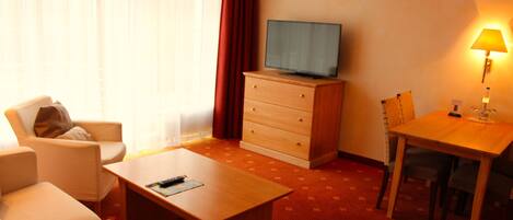 Una habitación de hotel con un escritorio de madera, un televisor en una cómoda, una silla, una mesa y una lámpara.