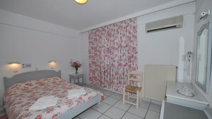 A bedroom with a bed, a chair, a small table, a radiator, and a mirror. - King Thiras (Santorini)
