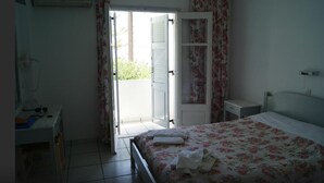 A bedroom with a bed, a desk, a wardrobe, and an open door leading to a balcony. - King Thiras (Santorini)