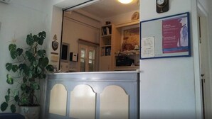 A reception area with a counter, a potted plant, a coat rack, and a bulletin board with an exhibition notice. - King Thiras (Santorini)