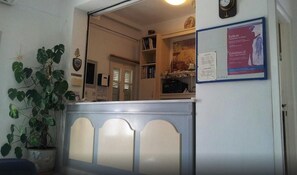 A reception area with a counter, a potted plant, a coat rack, and a bulletin board with an exhibition notice. - King Thiras (Santorini)