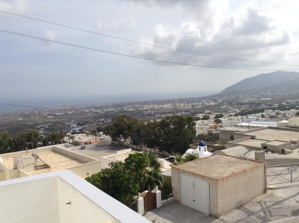 A residential area with buildings, some with flat roofs and others with sloped roofs, and a distant view of a coastline. - King Thiras (Santorini)