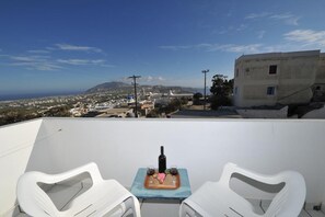 A rooftop terrace with a table set for two, overlooking a coastal town. - King Thiras (Santorini)