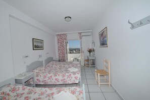 A bedroom with two beds, a desk, a chair, and a window with a view. - King Thiras (Santorini)