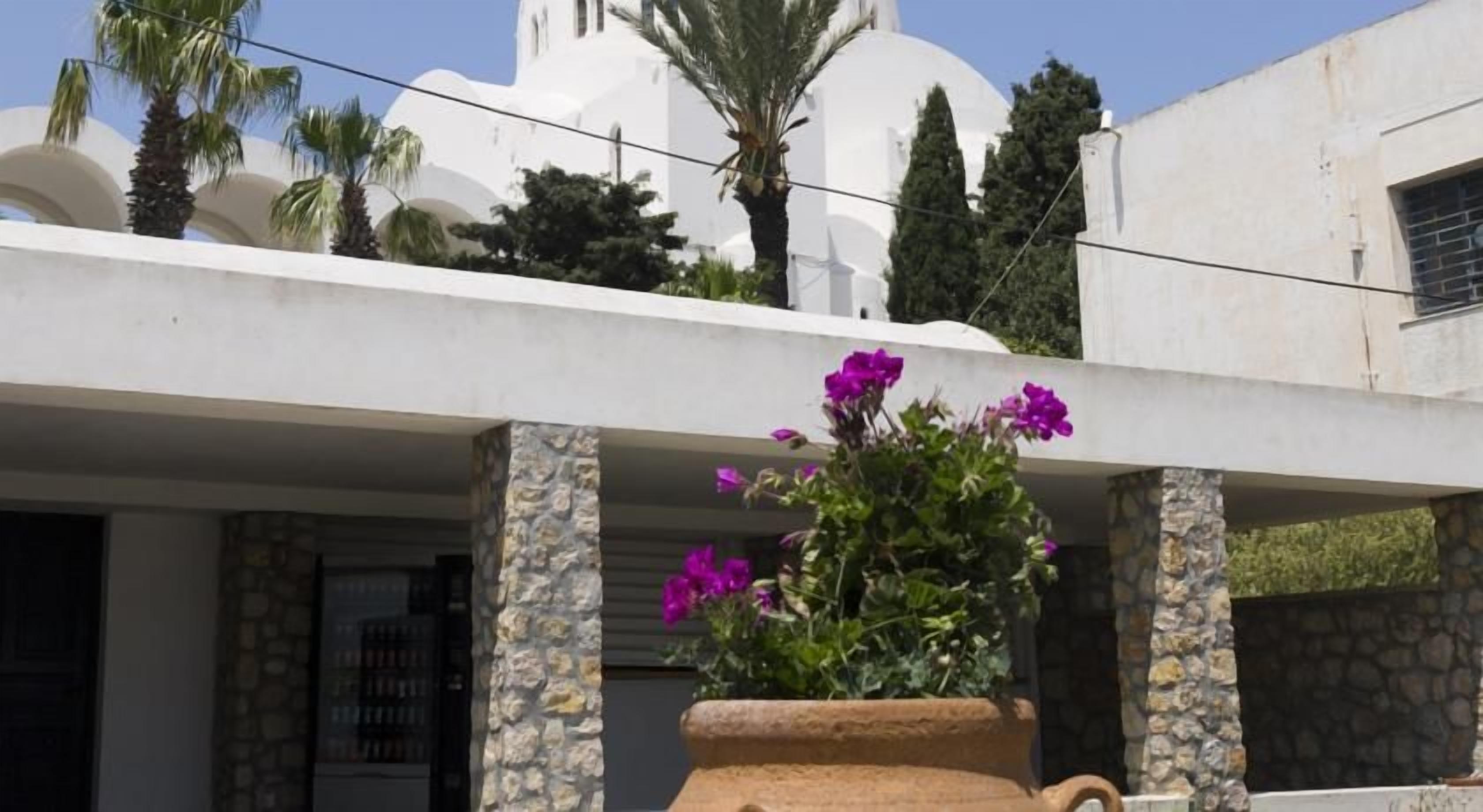 A building with a white facade, stone pillars, and a large flower pot with purple flowers.