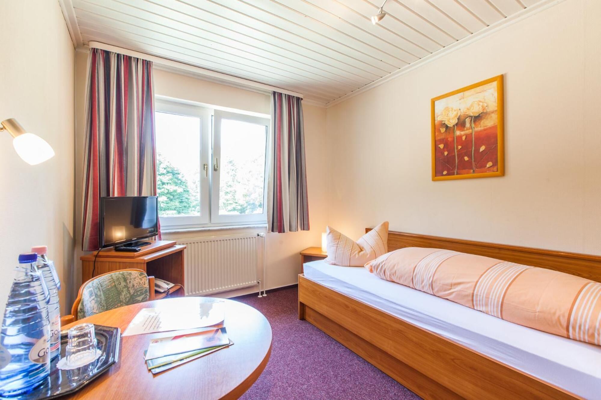 A hotel room with a bed, a TV, a desk with a chair, a table with a tray, and a window with curtains.
