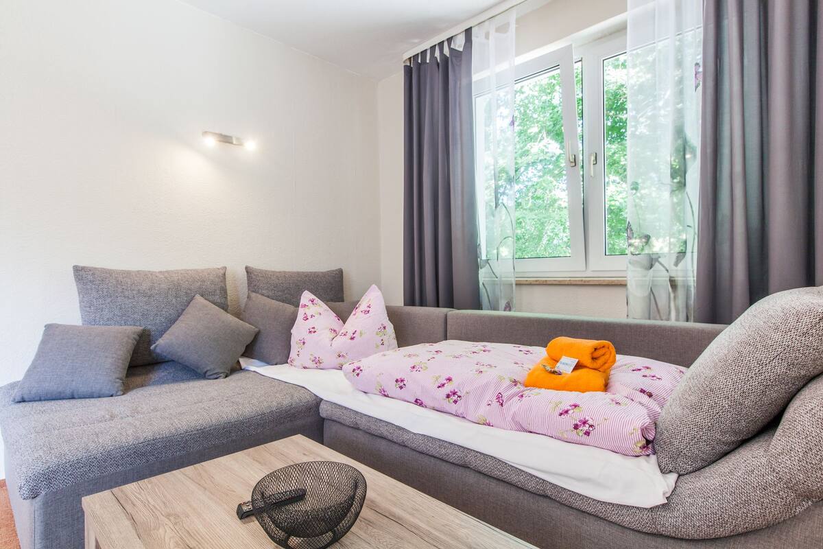 Una sala de estar moderna con un sofá gris, una mesa de centro de madera y una ventana con cortinas.