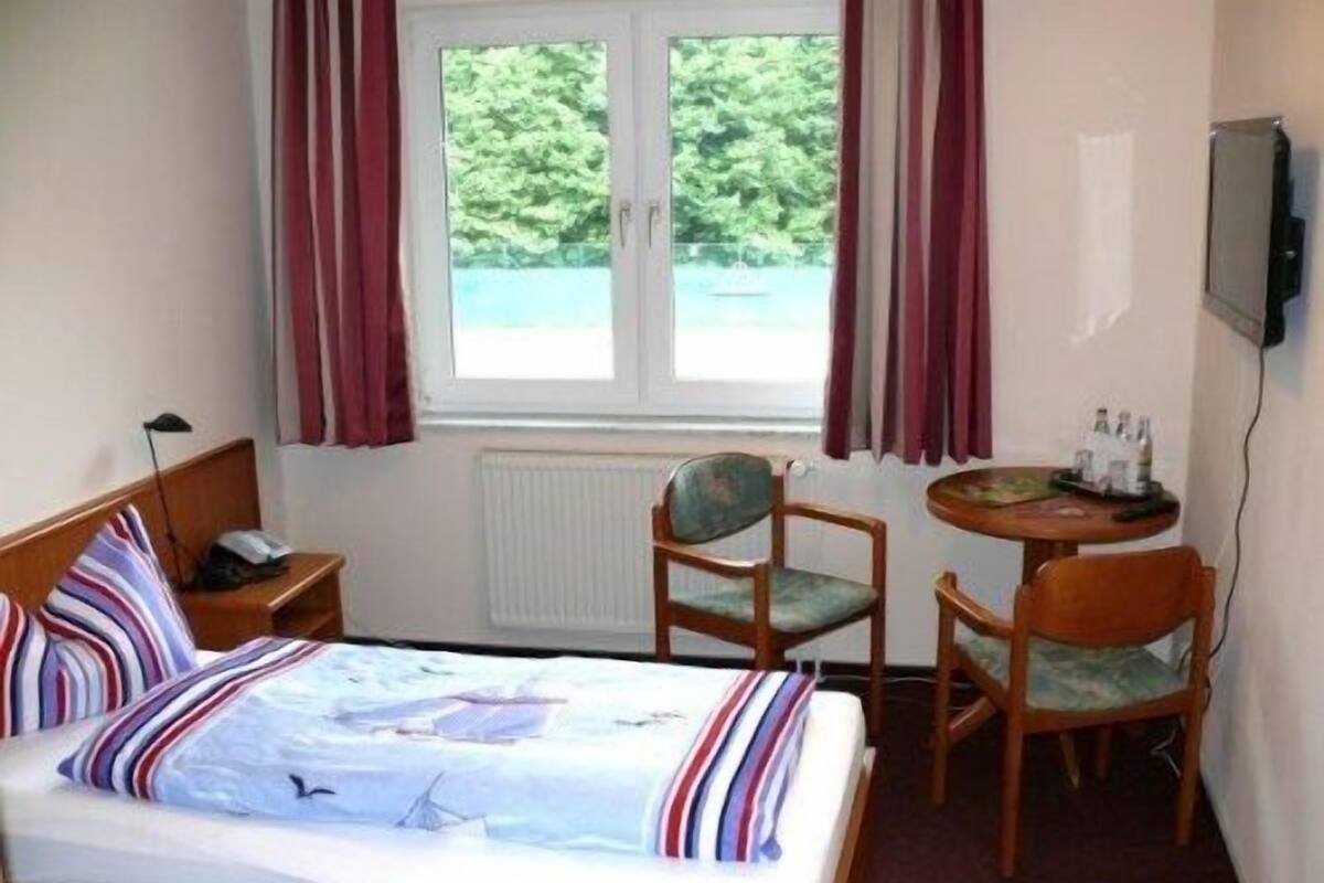 Habitación de hotel con cama, dos sillas, una mesita, televisor y ventana con cortinas.