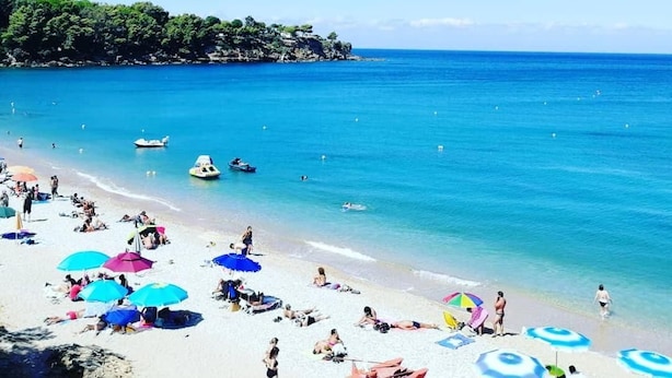 Una playa con aguas azul turquesa, gente tomando el sol y barcos.