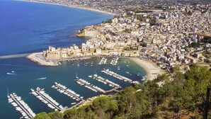 Un paisaje urbano costero con un puerto deportivo lleno de barcos, rodeado de edificios apretados y montañas al fondo.