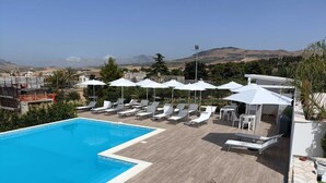 Una piscina con tumbonas y sombrillas, rodeada de una terraza de madera y vistas a colinas distantes.