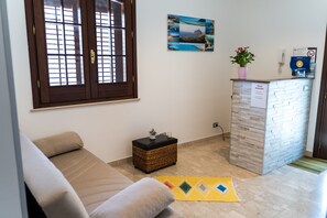 Ein Wohnzimmer mit einer Couch, einem kleinen Tisch mit Pflanze, einem Wandbild und einer Rezeption mit Schild.