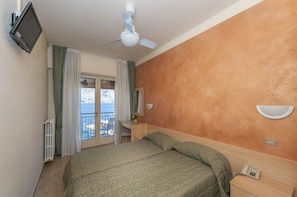 Ein Hotelzimmer mit Bett, Schreibtisch, Stuhl, Fernseher, Deckenventilator und Meerblick durch eine Balkontür.