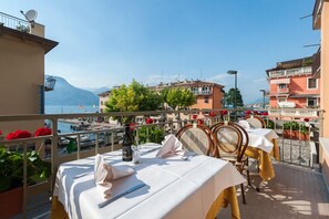 Eine Terrasse mit Essplätzen, mit Blick auf einen Yachthafen und Häuser mit Balkonen, unter blauem Himmel.