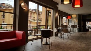A spacious indoor area with a red sofa, multiple tables and chairs, and large windows offering a view of the outside buildings. - Hotel Sorriso (Brenzone sul Garda)