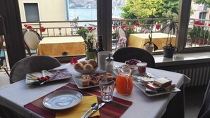 A table set with breakfast items, including eggs, bread, and juice, overlooking a scenic coastal view. - Hotel Sorriso (Brenzone sul Garda)