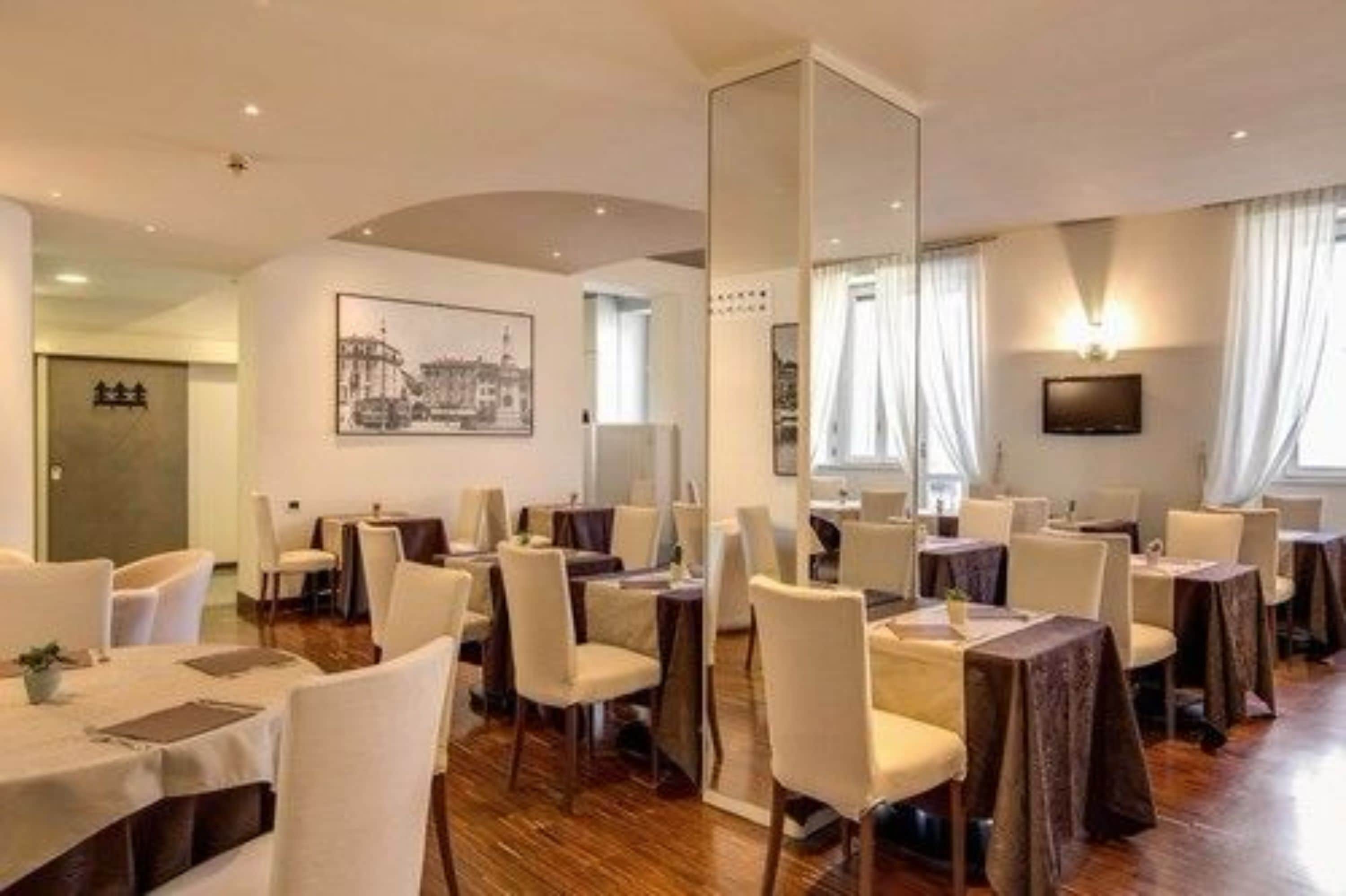 Een restaurantgedeelte in een hotel met ronde tafels, witte stoelen en een grote spiegel.