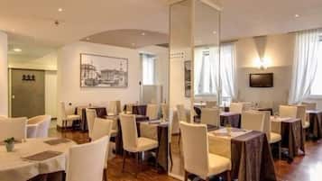 Une salle à manger d’hôtel avec des tables rondes, des chaises blanches et un grand miroir.