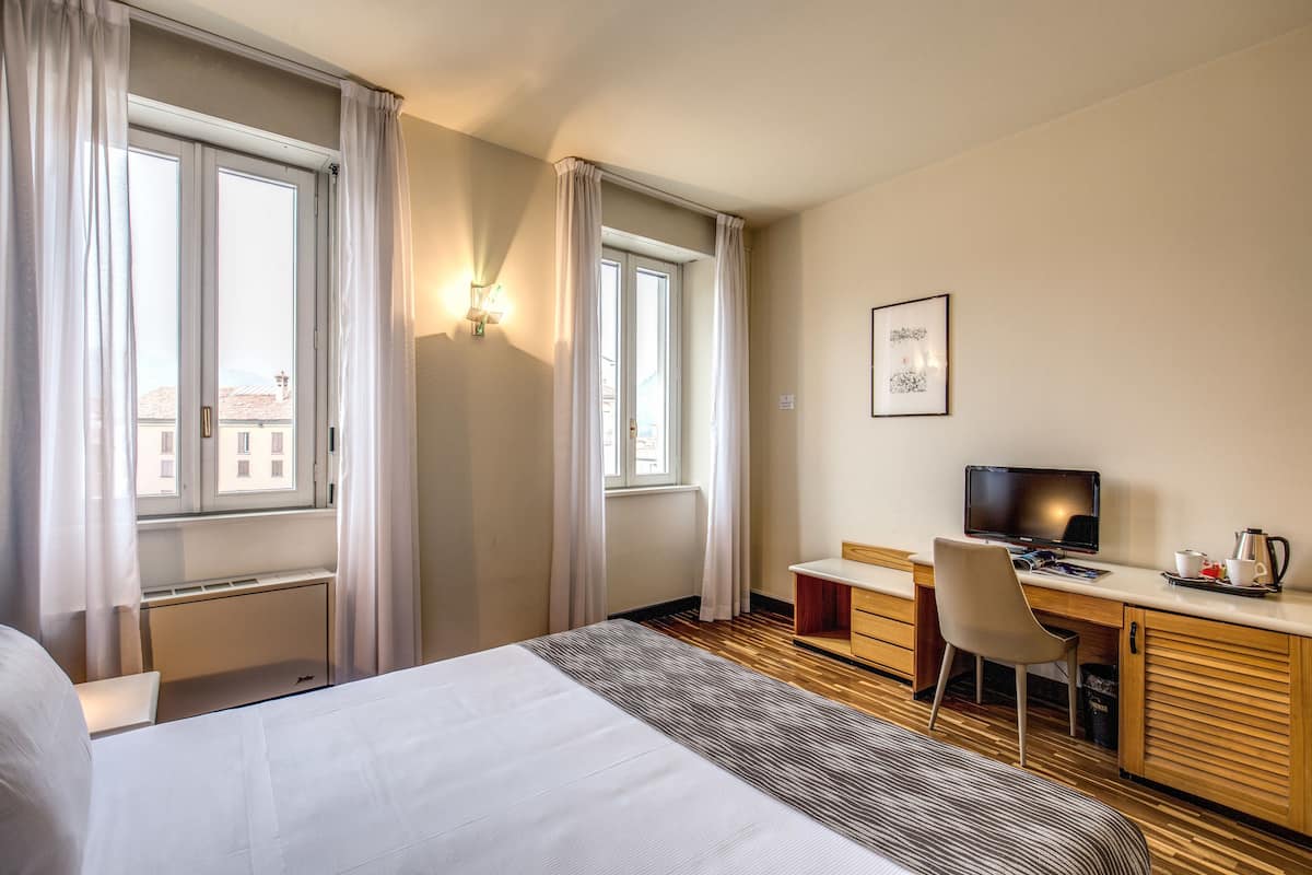 Habitación de hotel con cama, escritorio, silla, televisión y ventana con cortinas.