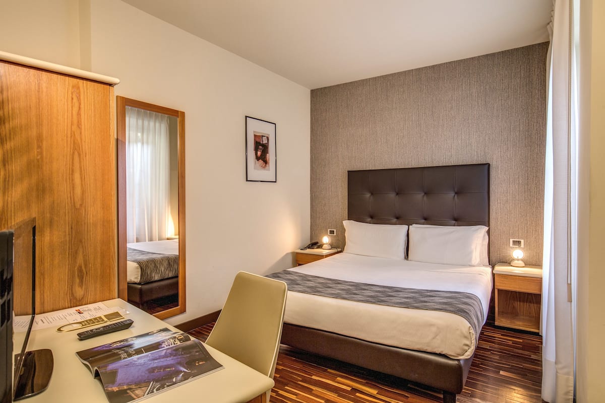 Habitación de hotel con una cama grande, un escritorio con una silla, un televisor y un armario de madera.