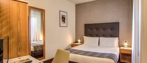 Habitación de hotel con una cama grande, un escritorio con una silla, un televisor y un armario de madera.