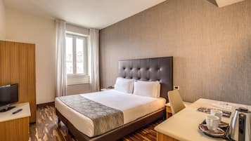 A hotel room with a large bed, a TV, a desk with a coffee maker, and a window with curtains.