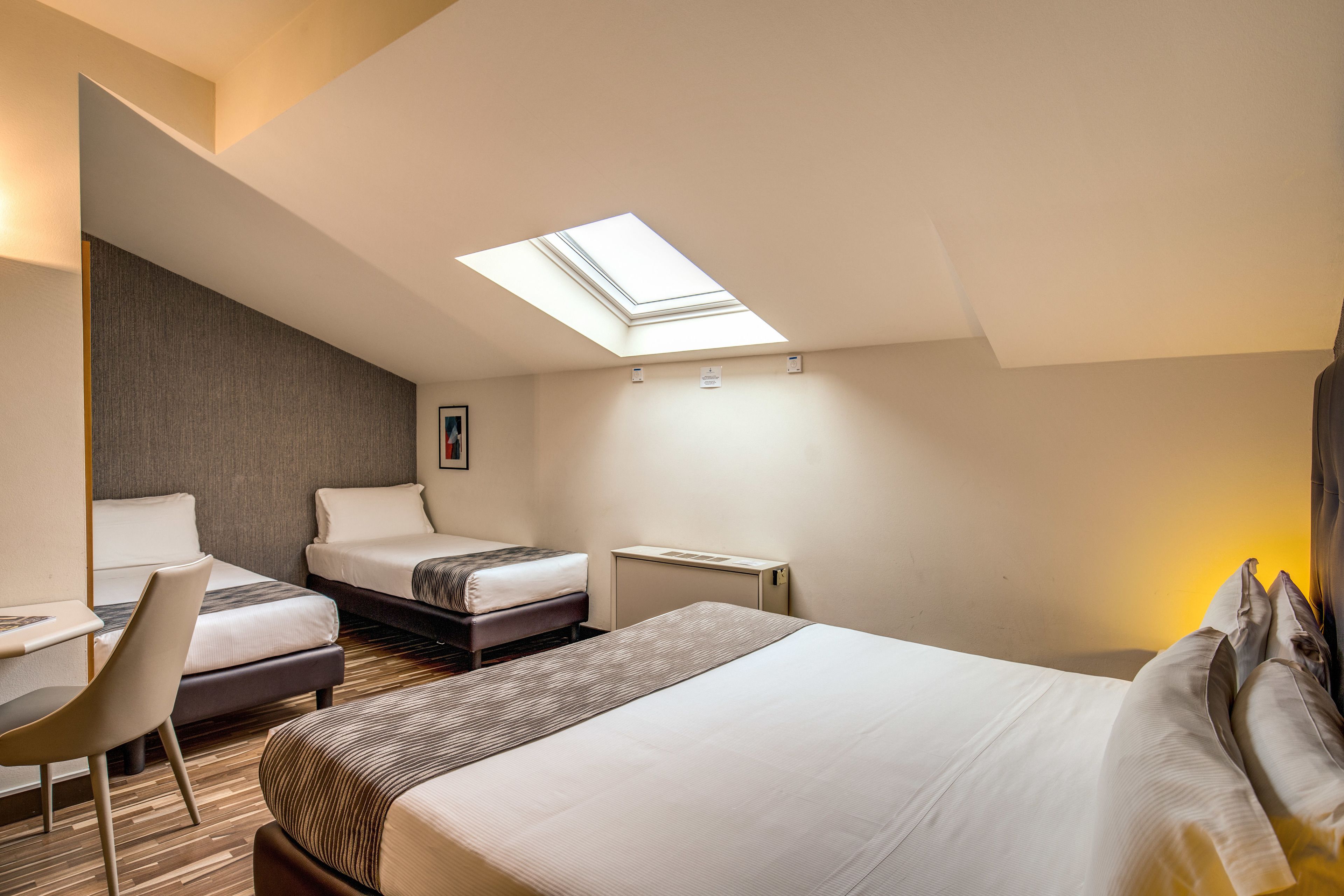Ein Hotelzimmer mit Oberlicht, zwei Betten, einem Schreibtisch und einem Stuhl.