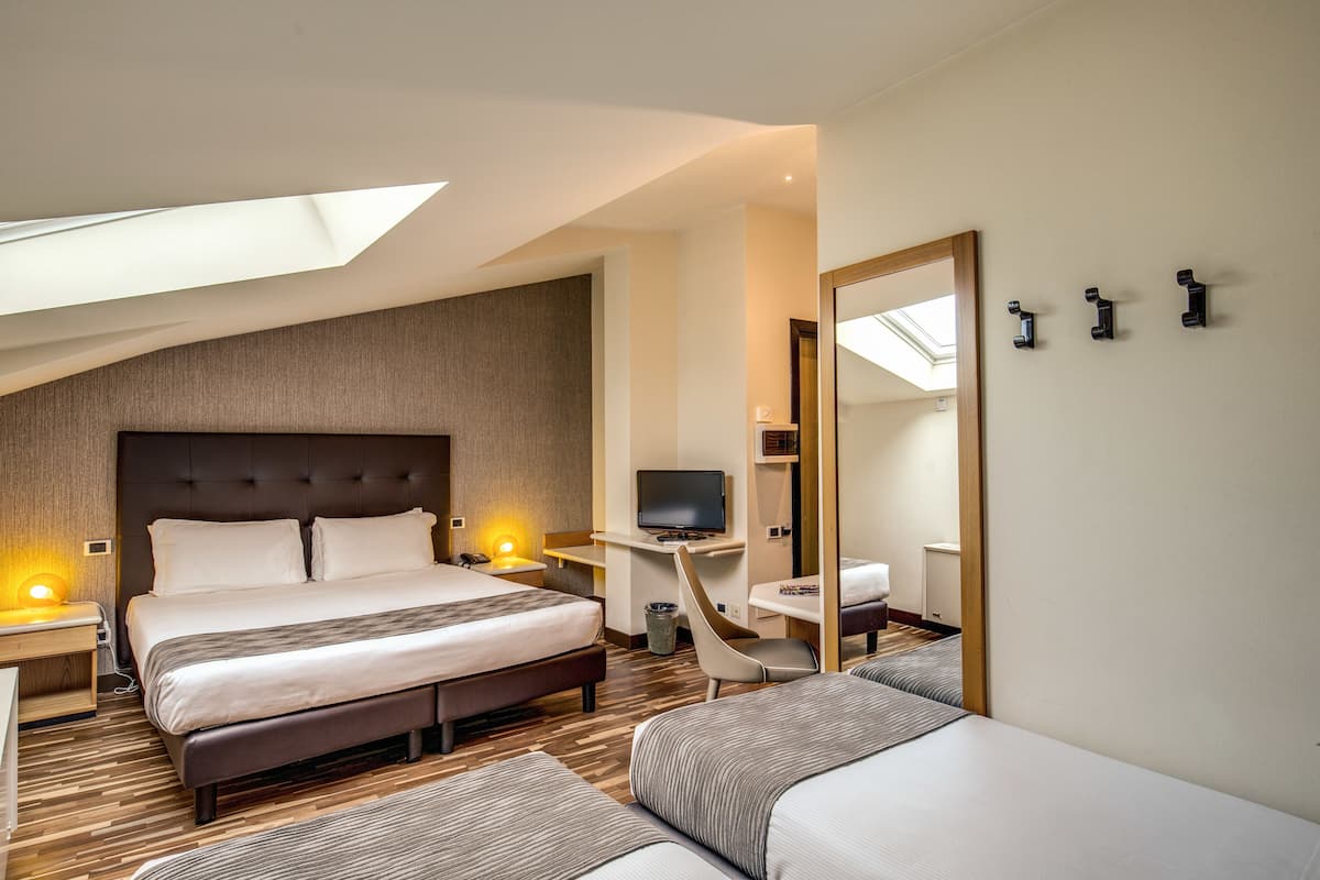 Una habitación de hotel moderna con una cama grande, un escritorio con televisor, una silla y un espejo.