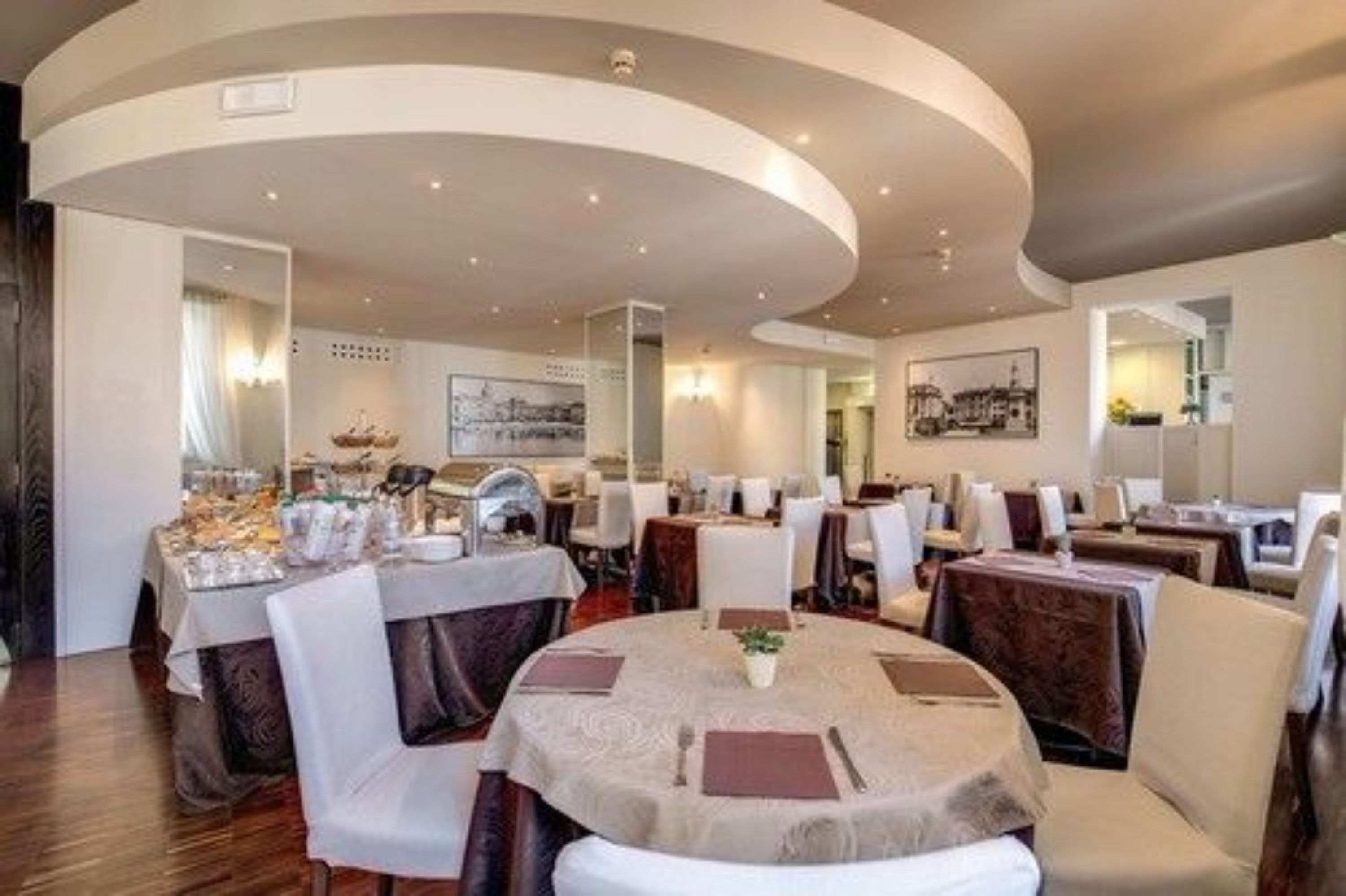 Un restaurante con mesas redondas, sillas blancas y un techo curvo.