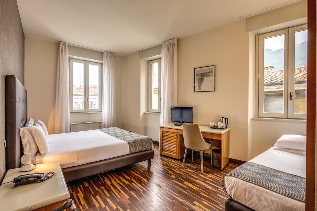 Una habitación de hotel con dos camas, un escritorio, una silla, un televisor y una ventana con cortinas.