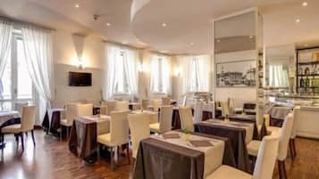 Un comedor de hotel con mesas y sillas, una barra y un ventanal con cortinas.