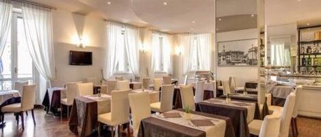 A hotel dining area with tables and chairs, a bar, and a large window with curtains.