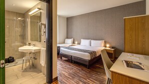 A hotel room with a shower, a sink, a bed with two pillows, a bedside table with a lamp, and a chair. - Albergo Firenze (Como)