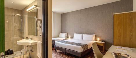 A hotel room with a shower, a sink, a bed with two pillows, a bedside table with a lamp, and a chair.