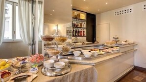 A buffet setup with various food items and beverages, a counter with a display of bottles, and a window with curtains. - Albergo Firenze (Como)