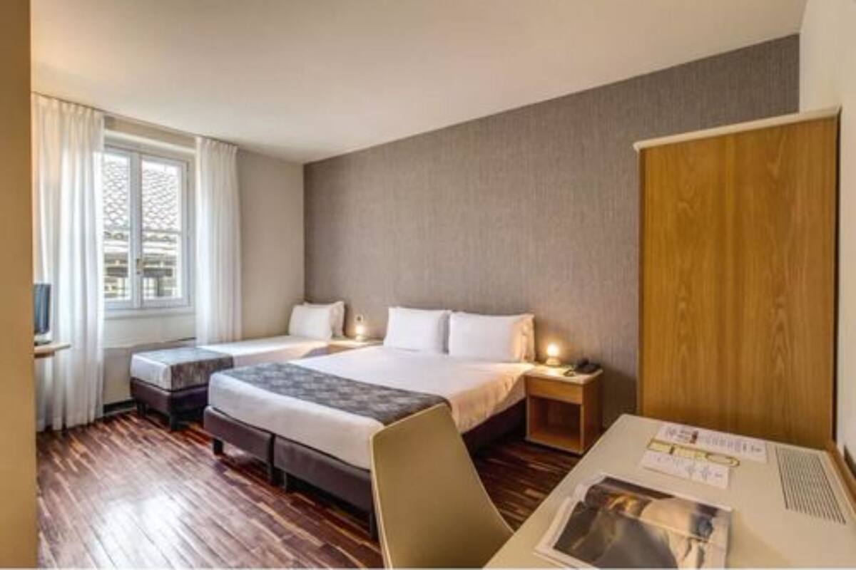 Una habitación de hotel con una cama grande, un escritorio con una silla y una ventana con cortinas.