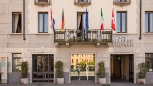 The exterior of the Albergo Firenze hotel with multiple flags, a grand entrance, and potted plants. - Albergo Firenze (Como)