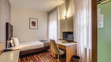Una habitación de hotel con cama, escritorio, silla, televisión y lámpara.