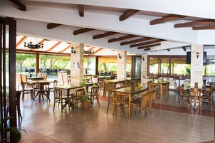 Un comedor interior espacioso con mesas y sillas de madera, ventanas amplias y un techo alto con vigas a la vista.