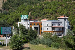 Hotel SPILOS, con un cartel, rodeado de vegetación y edificios modernos.